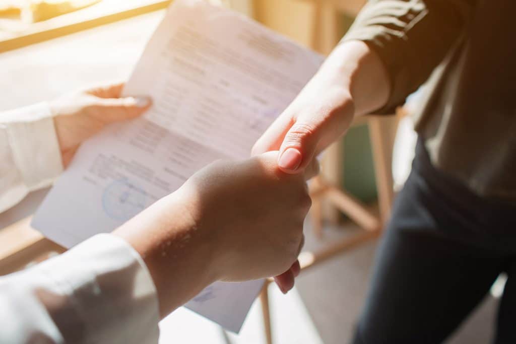 dos mujeres dándose la mano y sujetando un papel